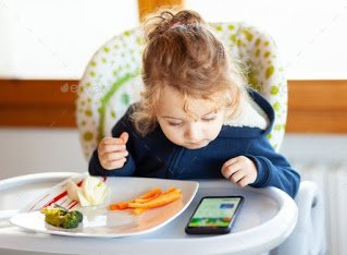Child playing with mobile while eating, Lost childhood